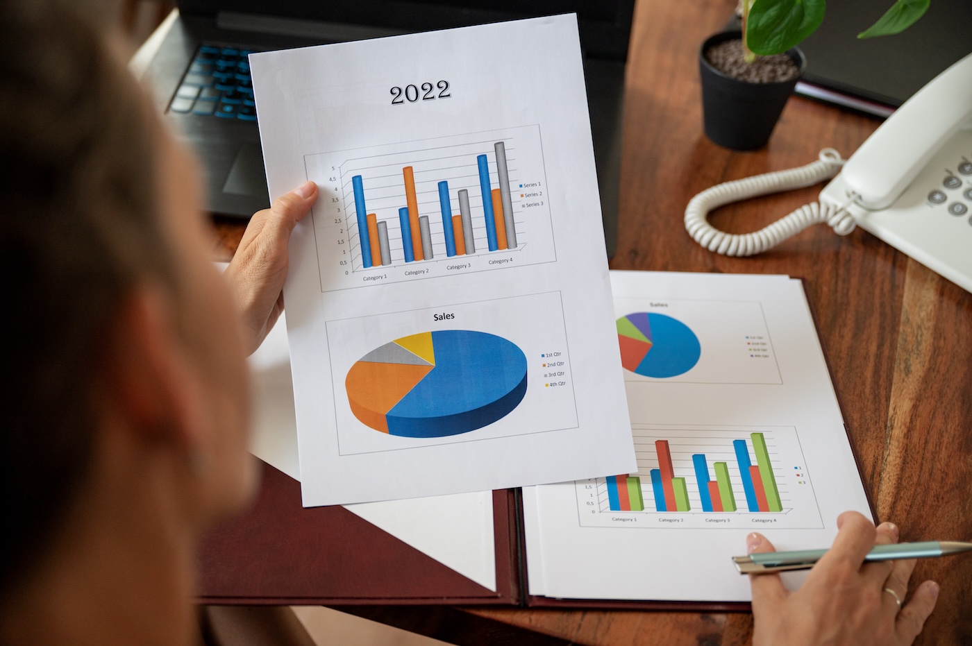 Overhead view of businesswoman reading and examining a statistical business report with colorful graphs and charts.